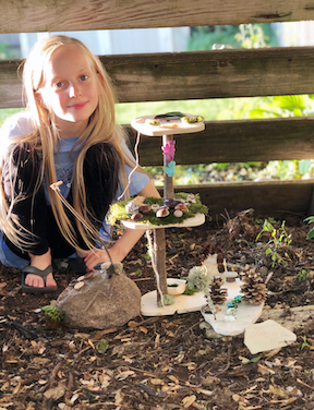 girl with her newly-made fairy house in her yard.