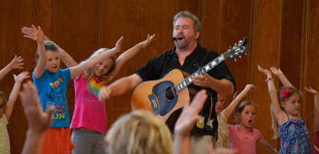 Singer Randy Peterson surrounded by kids smiling and dancing with arms up