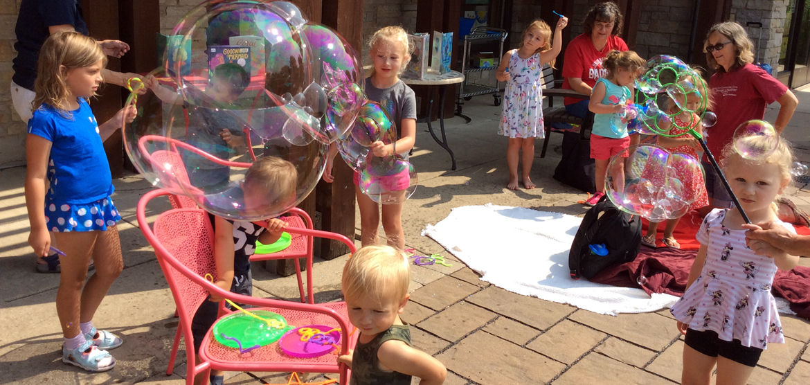 Small children playing with bubble wands in front of library.