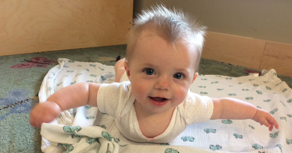 Baby Lucy on tummy, smiling at camera, on the storytime room floor looking cute.