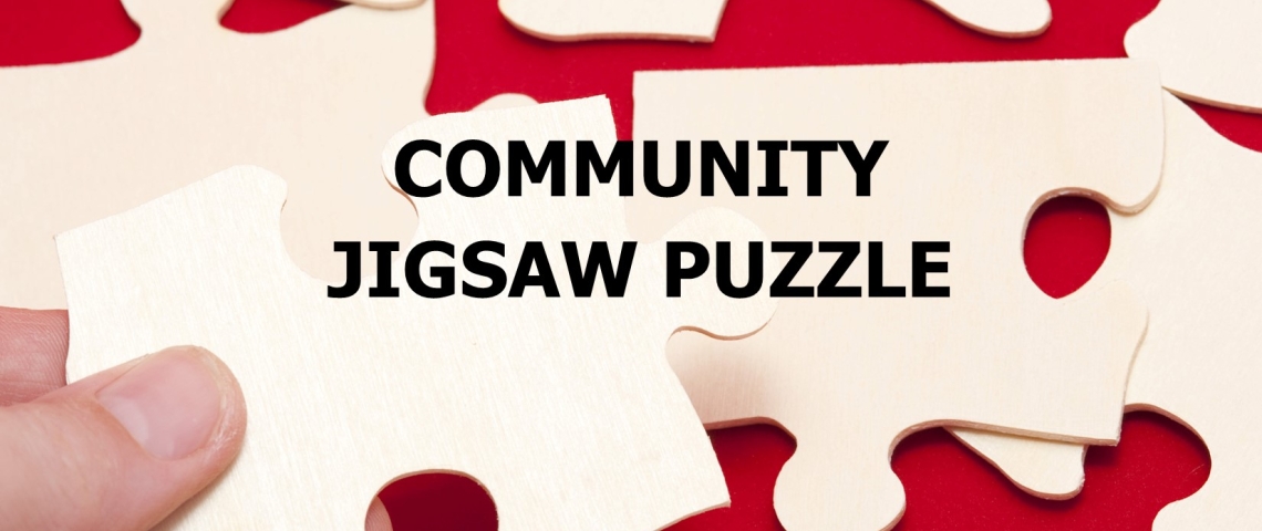 Image of a hand holding a jigsaw puzzle piece to be fitter into a puzzle in the background.  Puzzle pieces are plain white and the background is red.