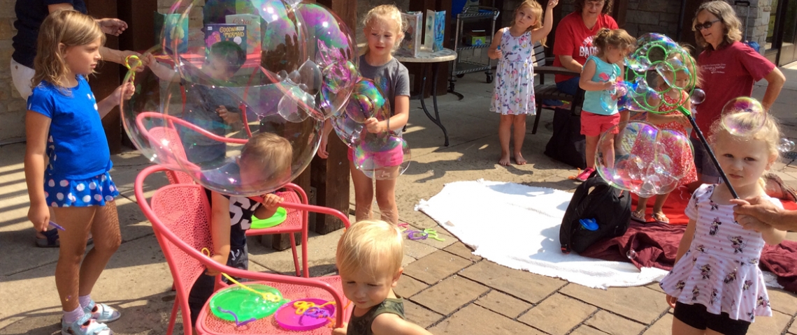 Small children playing with bubble wands in front of library.